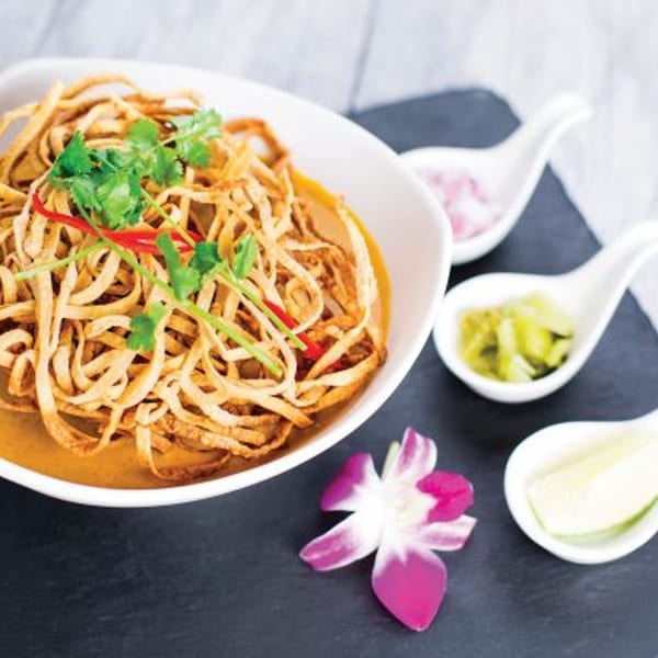 Noi Thai Cuisine's Khao Soi, a noodle dish with crispy noodles, cilantro, and chili, with sides.