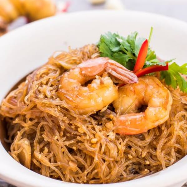 Glass noodles with shrimp, garnished with cilantro and red chili, served in a white bowl.