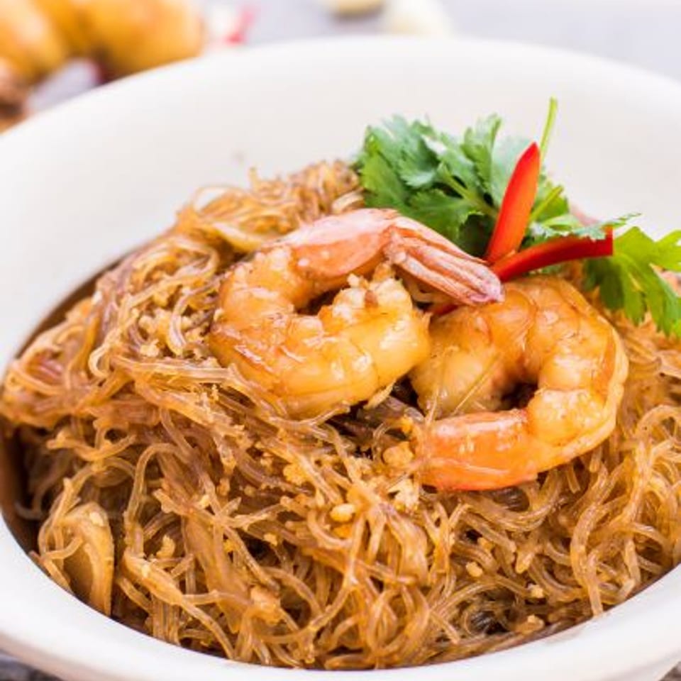 Glass noodles with shrimp, garnished with cilantro and red chili, served in a white bowl.